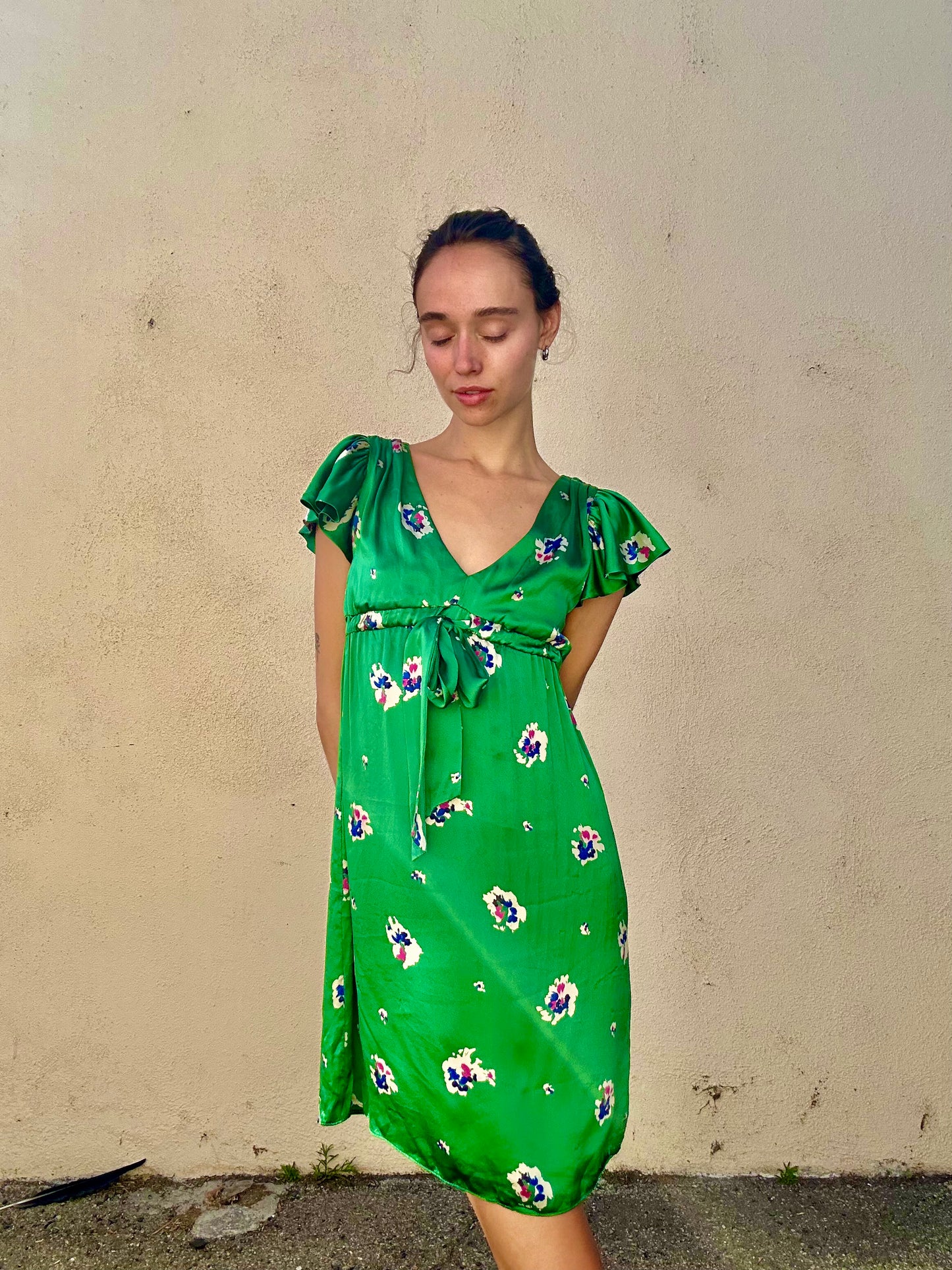 Woman wearing a green floral dress against a plain wall.