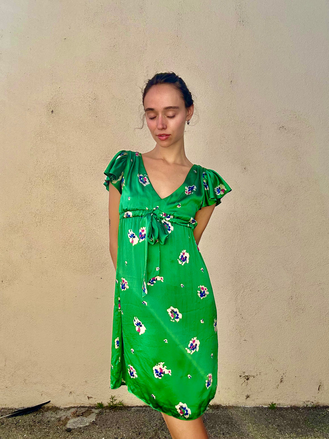 Woman wearing a green floral dress against a plain wall.