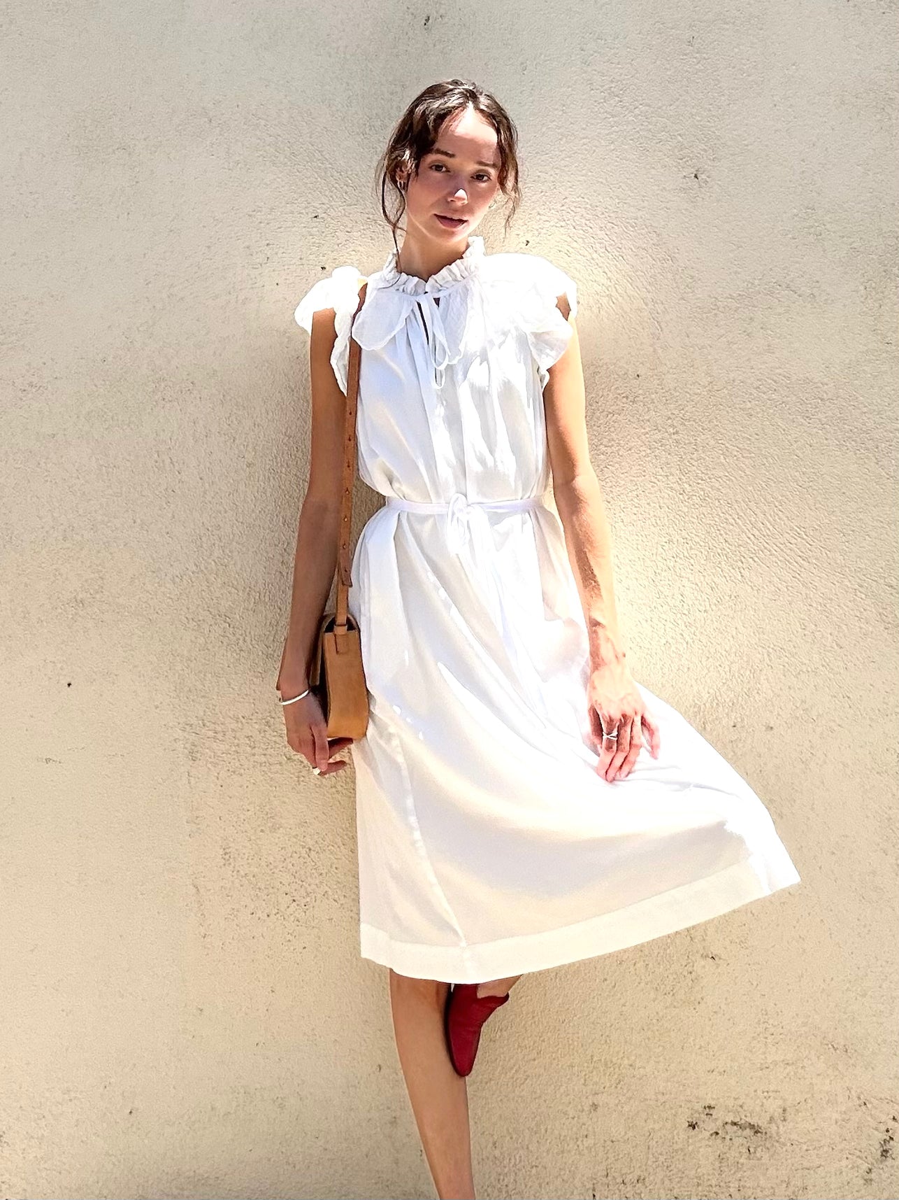 Woman wearing a white dress against a plain wall