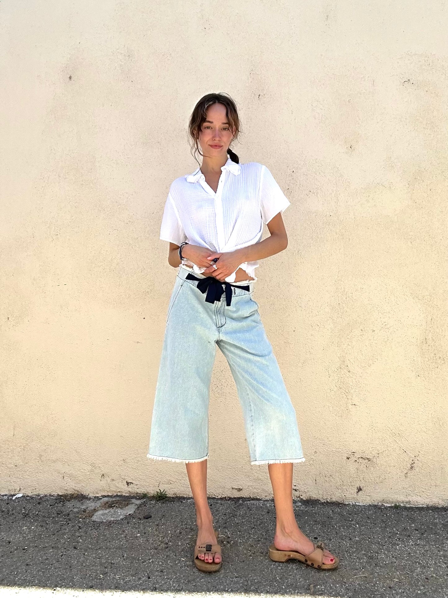 Person wearing a white shirt and light blue jeans against a beige wall.
