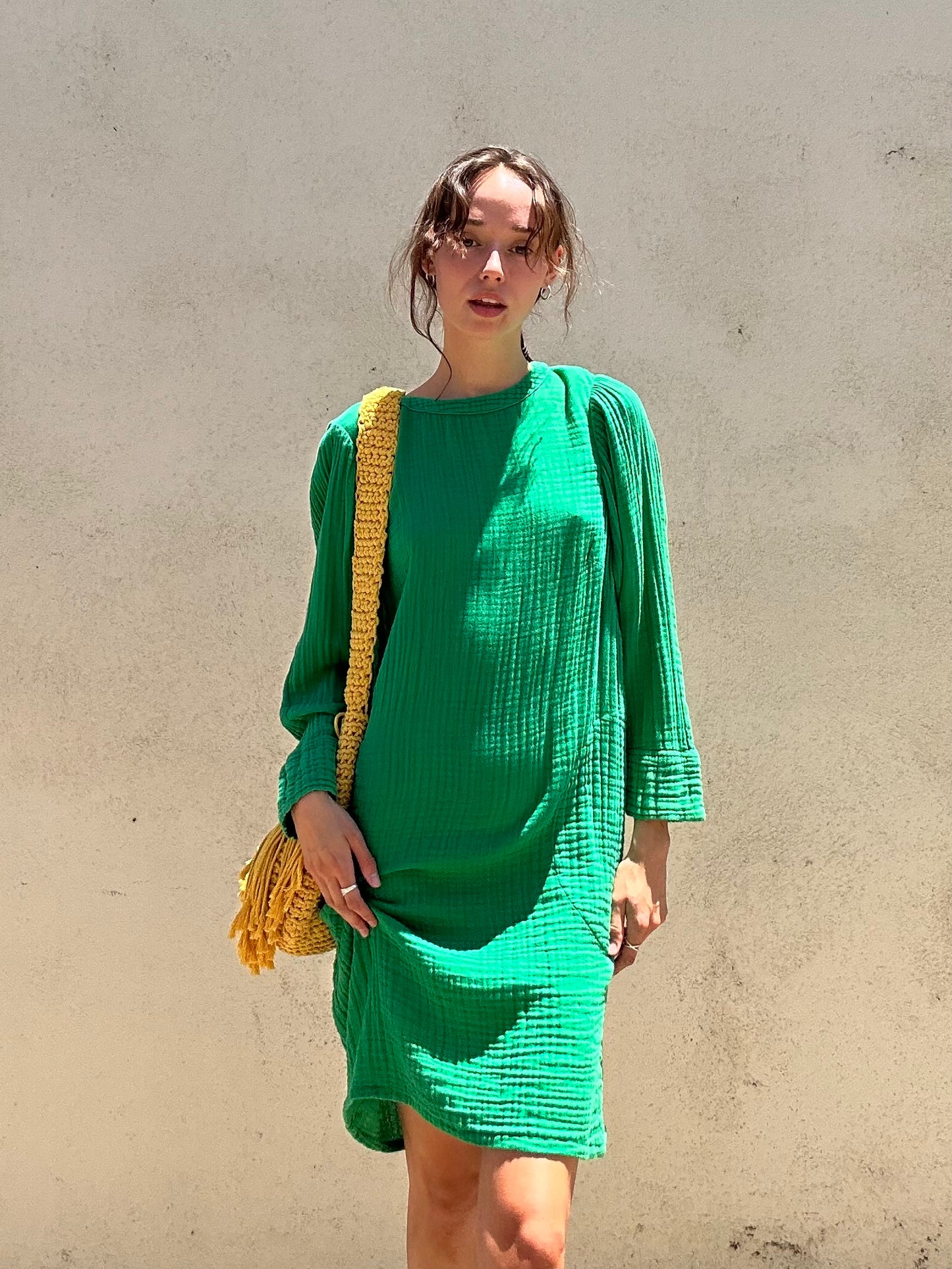 Woman wearing a green dress with a yellow bag against a plain background