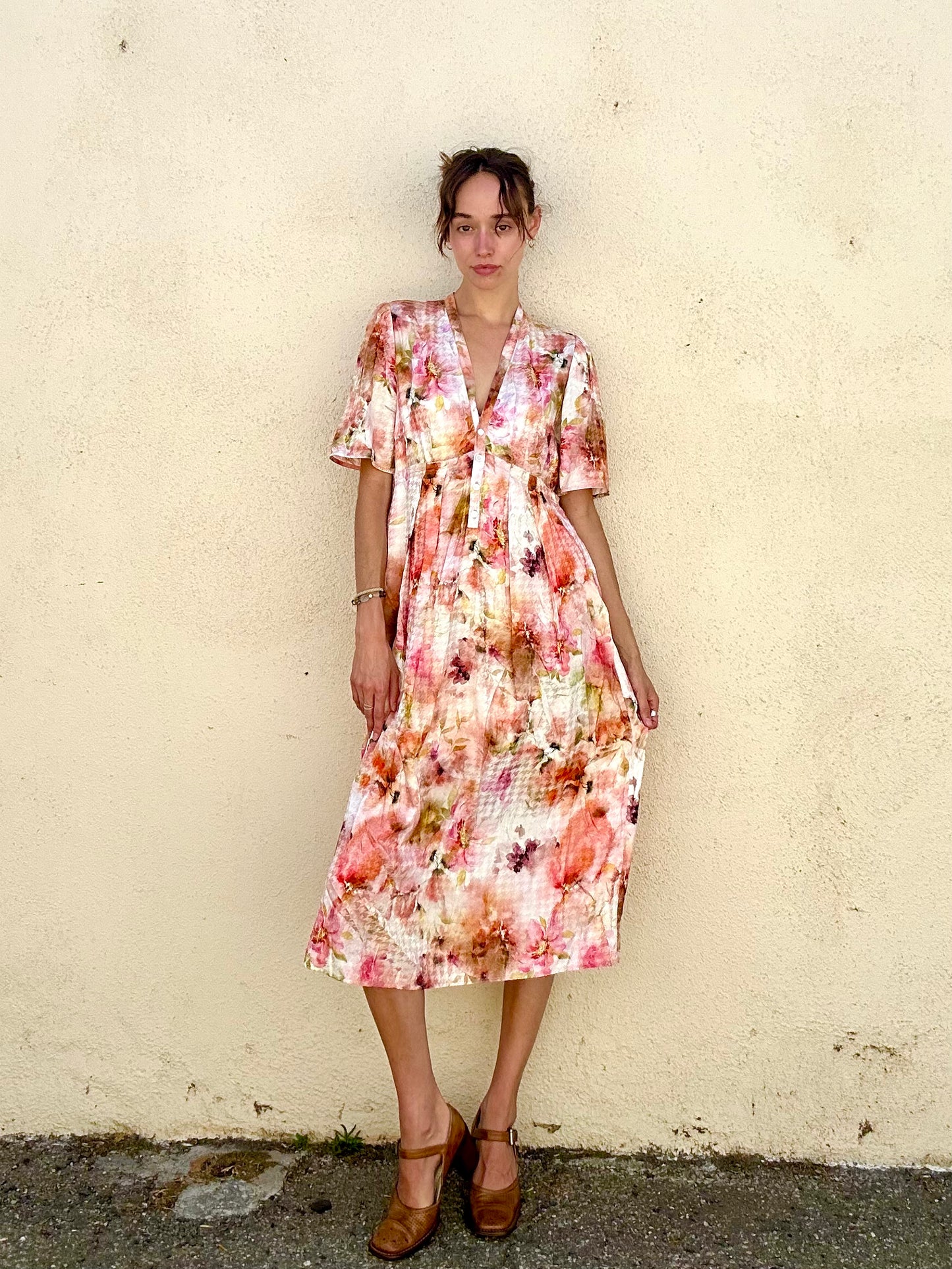 Woman wearing a floral dress standing against a plain wall.