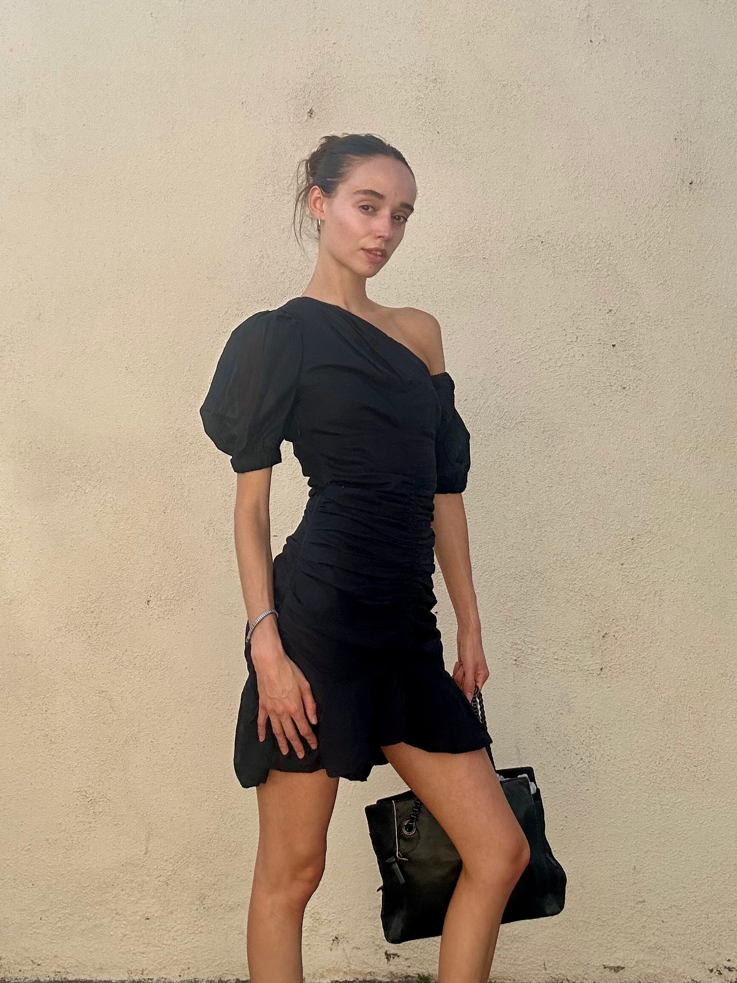 Woman wearing a black off-shoulder dress against a beige wall