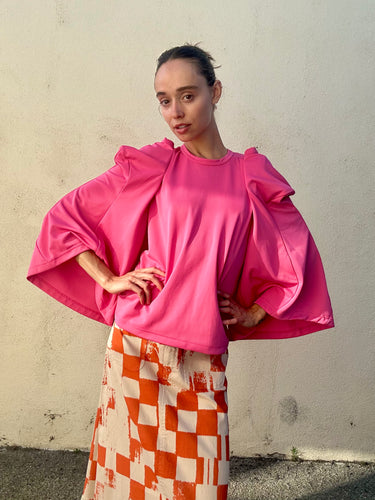Person wearing a bright pink top with puffed sleeves and a patterned skirt against a plain background