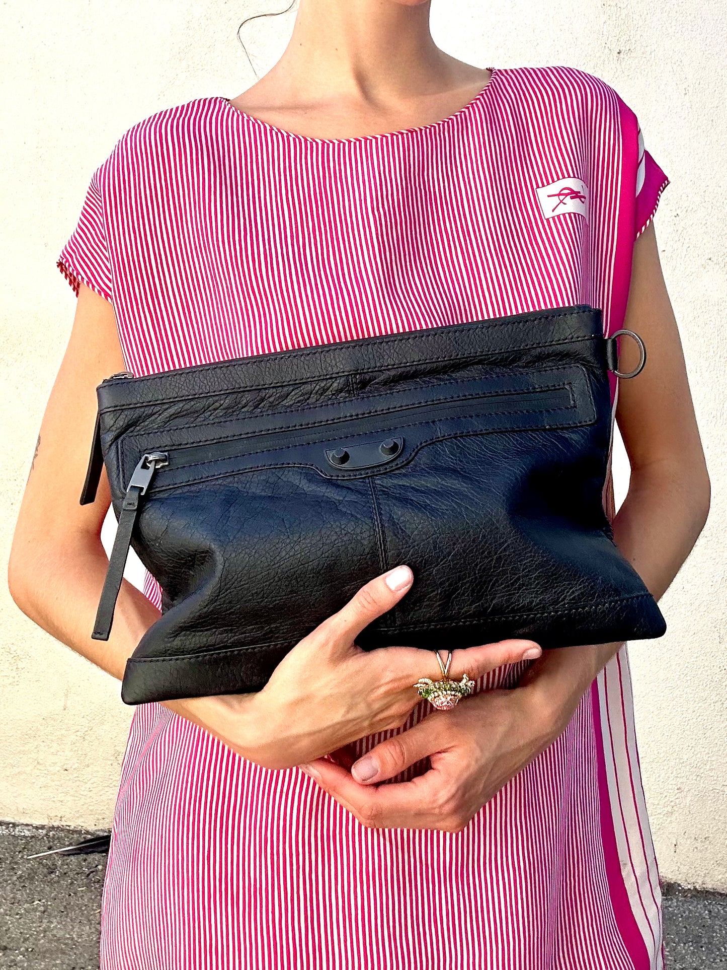 Person holding a black clutch bag against a neutral background