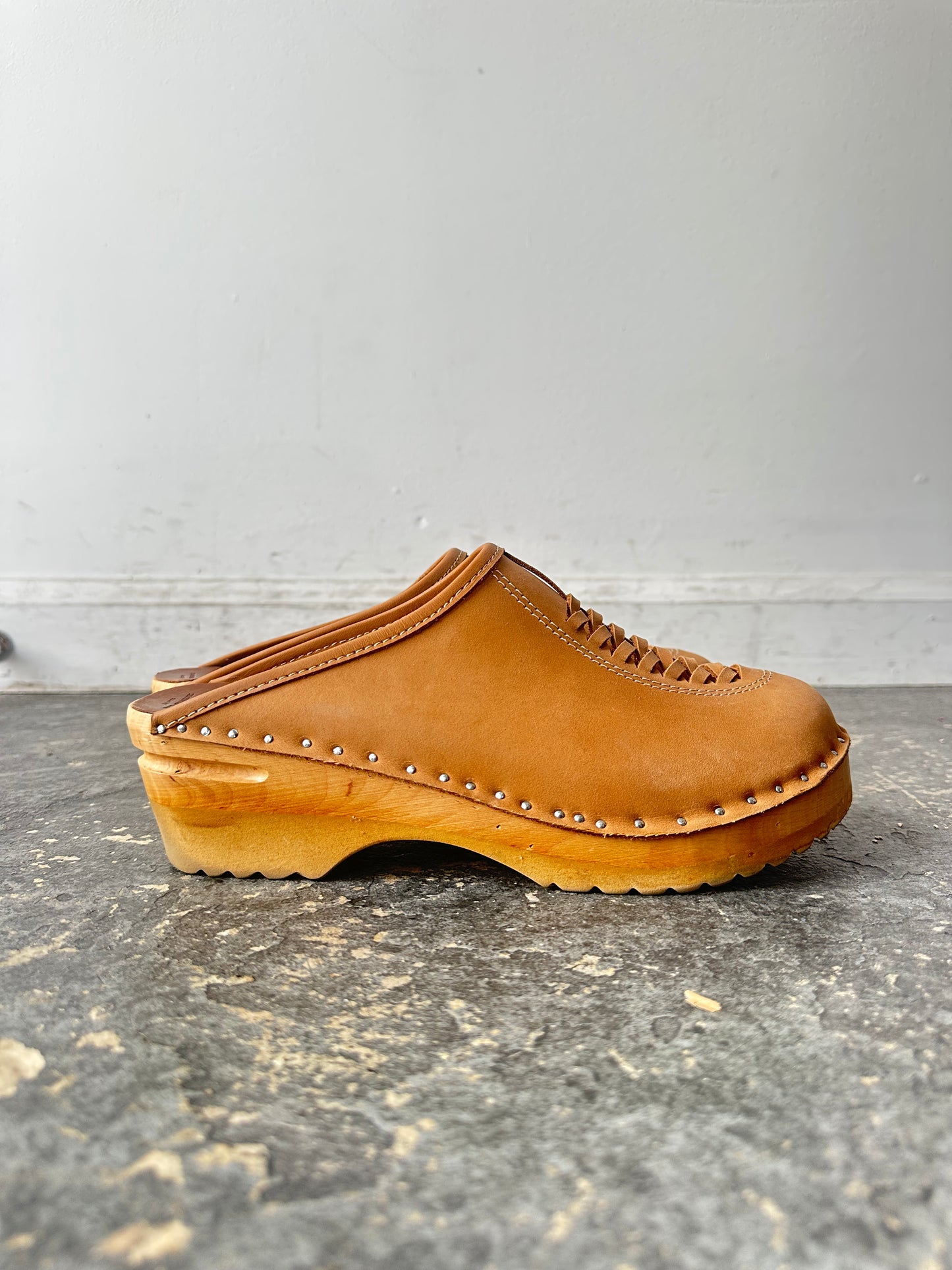 Brown wooden clog shoe on a gray surface with a white background