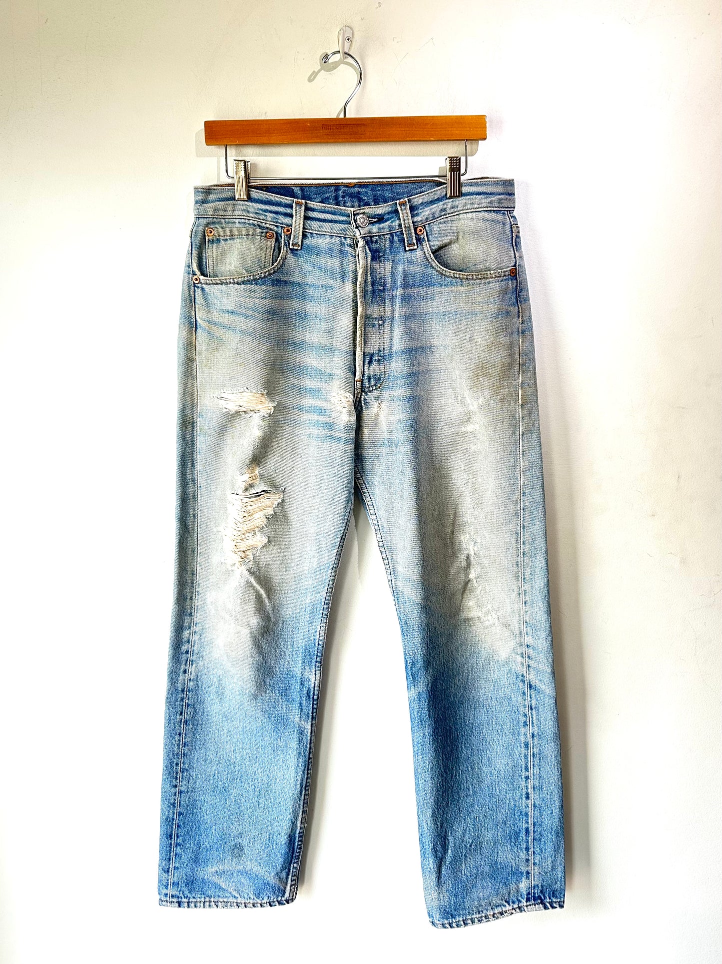 Distressed blue jeans on a hanger against a white background