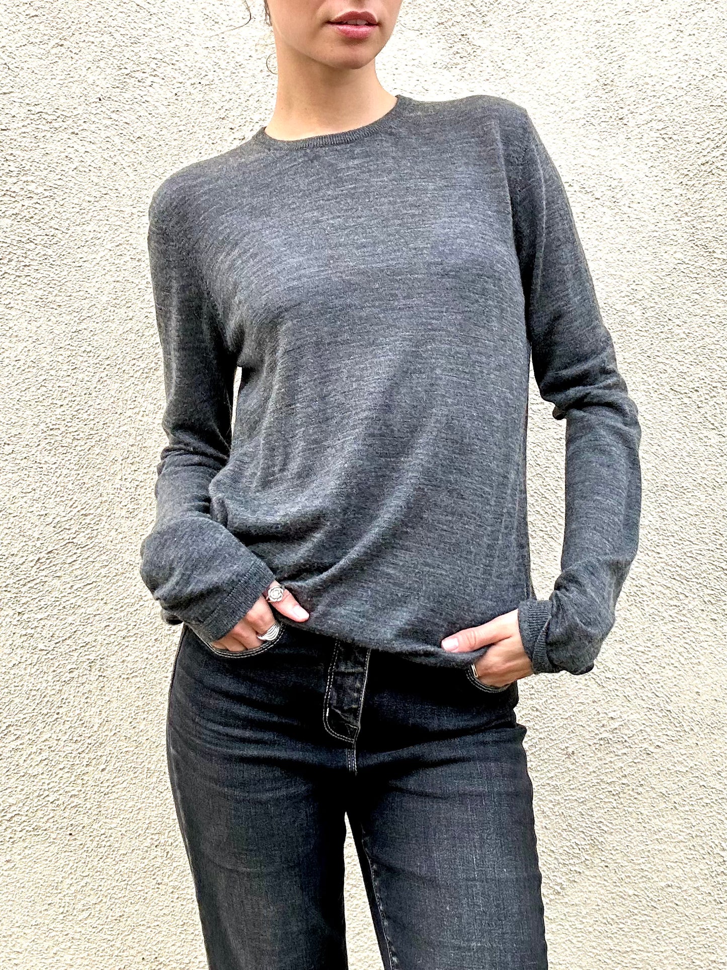 Person wearing a gray long-sleeve shirt and dark jeans against a light background