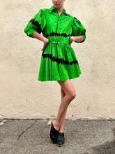 Person wearing a green dress with black accents against a beige wall.