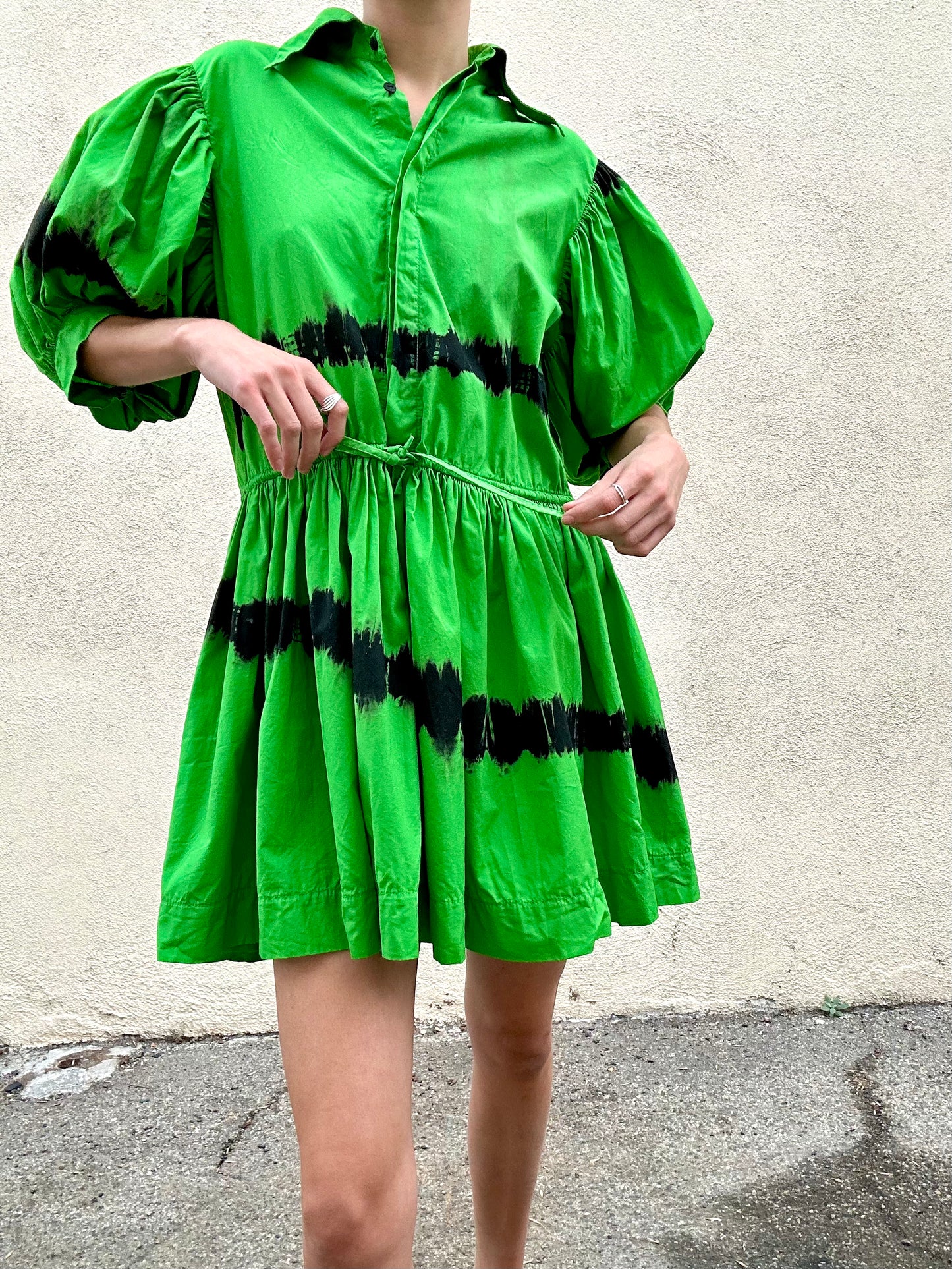 Green dress with black tie-dye patterns worn by a person against a plain background