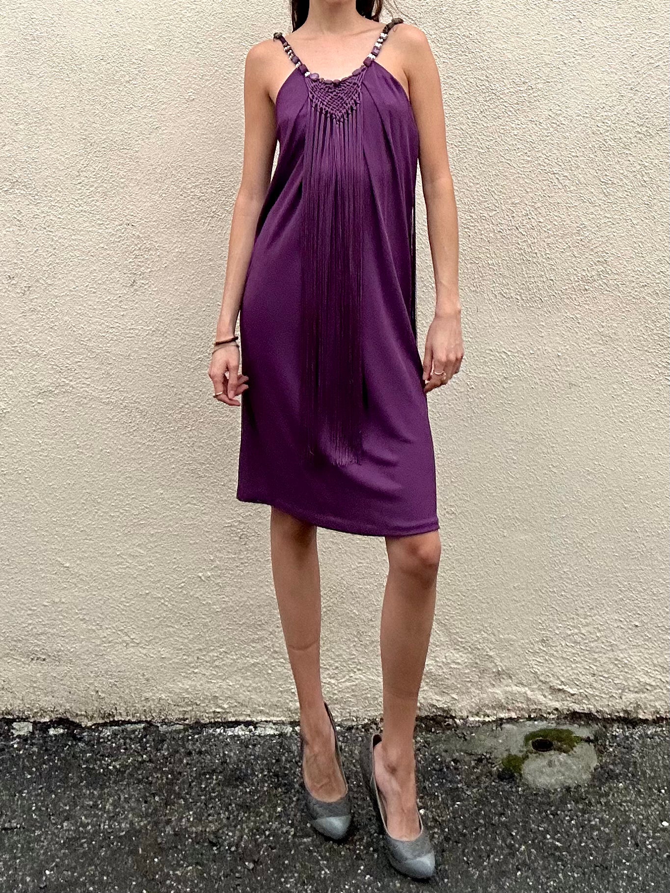 Person wearing a purple dress with a textured neckline against a beige wall.